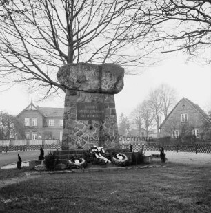 Tremsbüttel-Dorf: Dorfplatz mit Bäumen: Ehrenmal mit Kränzen: im Hintergrund Wohn- und Bauernhäuser
