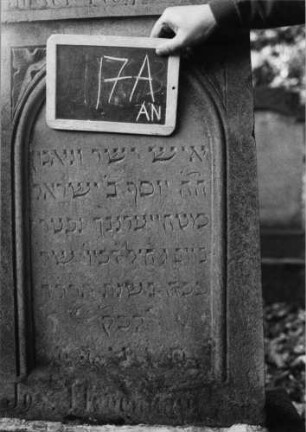Grabstein 17 (Index: 99801907) Material: Sandstein Zustand: verwittert Maße HxBxT: 156x52x15 cm Beschreibung: Stele, getreppter Sockel, Giebel mit Eckakroteren, eingetieftes Schriftfeld mit Rundbogen Symbolik: Stern, Blätter: Grabstein 17A