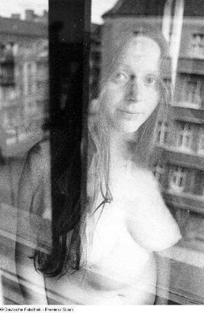 Weiblicher Akt in einem Raum (halbfigurig), fotografiert hinter einem Fenster mit Spiegelung der äußeren Umgebung
