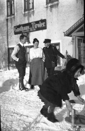 Welsberg (Bozen)? Gasthaus zum Tiroler (Teilansicht), davor Ehepaar (Familie Hell?) (im Vordergrund Kind mit Schlitten) mit Briefträger
