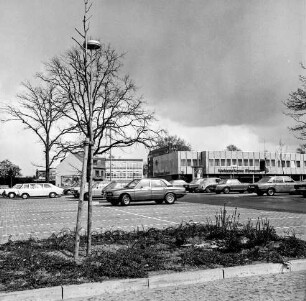 Markt: vorn Parkplatz mit Pkws: dahinter Einkaufszentrum mit Filiale der Kreissparkasse Stormarn: links Bäume