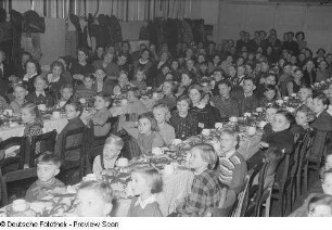 Kinder und Mütter an einer gedeckten und geschmückten Tafel bei der Weihnachtsfeier des Verlags Volk und Wissen