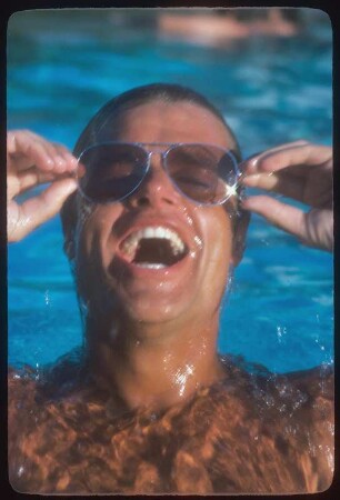 Modeaufnahme für Sonnenbrillen : Männliches Model mit silberner Brille, lachend, im Wasser schwimmend