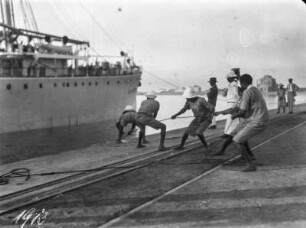 Vertäuen eines Schiffes : Männer vertäuen ein Schiff am Ufer