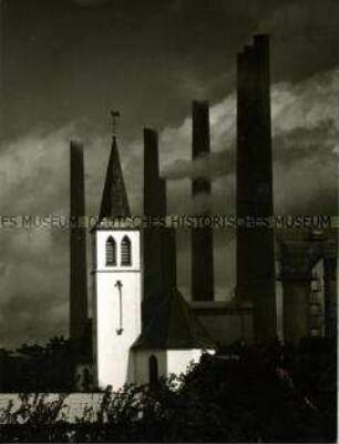 Heller Kirchturm umgeben von rauchenden Schornsteinen