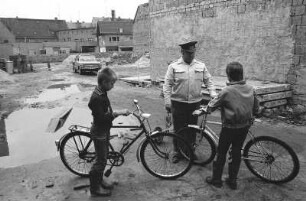 Polizist und Radjungen : Jungen die zuvor mit dem Fahrrad auf einer Baustelle und in Pfützen gespielt haben werden von einem Volkspolizisten (VP) angehalten und ermahnt