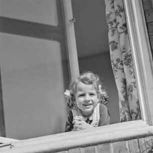 Mädchen mit Zöpfen und Schleifen schaut aus dem Fenster