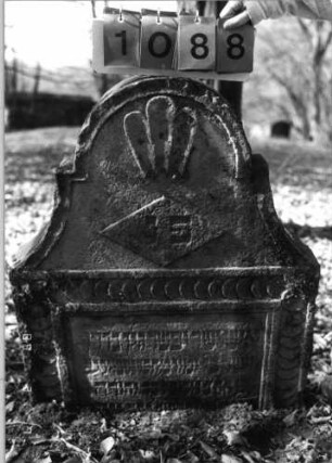 Grabstein 1088 (Index: 99753299) Material: Sandstein Zustand: verwitt/Stele eingesunken Maße HxBxT: 94x78x14 cm Beschreibung: Stele, doppelt eingezog. Rundbogenabschl. , rechteck. Schriftfeld eingetieft Symbolik: stilisierte Muschel, Raute, Scheibenfries: Grabstein 1088