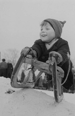 Kinder beim Ski- und Schlittenfahren, Junge liegend auf einem Schlitten