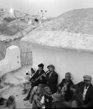 Romadorf, musizierende Männer sitzen mit Frau und Kindern vor einem Haus