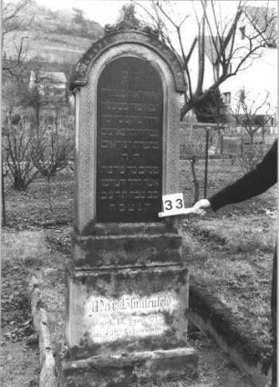 Grabstein 33 (Index: 99805068) Material: Sandstein mit schwarzer Marmorplatte Zustand: verwittert, Akroterion abgebrochen Maße HxBxT: 195x62x27 cm Beschreibung: Stele auf gestuftem Sockel mit Rundbogen und Mittelakroterion; Inschriftennische mit Rundbogen Symbolik: umlaufendes Fries, geschmücktes Akroterion: Grabstein 33
