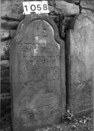 Grabstein 1058 (Index: 99630561) Material: Sandstein Zustand: stark verwittert mit Textverlust Maße HxBxT: 108x53x10 cm Beschreibung: Stele mit eingezogenem Rundbogenabschluß, Schriftfeld eingetieft: Grabstein 1058