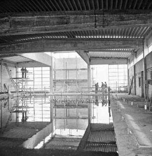 Hallenbad: Soltausredder: Rohbau: Innenansicht: vorn Schwimmbecken mit Wasser: hinten Arbeiter auf Leiter und Gerüst beim Innenausbau: dazwischen Baumaterial