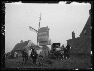 Nicht identifizierbare Ortschaft (Belgien/Nordfrankreich): Reiter und Pferdekarren vor landwirtschaftlichen Gebäuden, im Hintergrund eine Windmühle