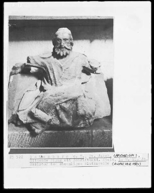Sitzende Figur mit Schriftband