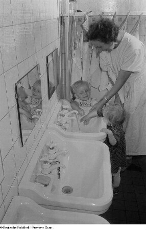 Zwei Kleinkinder und eine Erzieherin an einem Waschbecken eines Kinderkrippenbaderaum