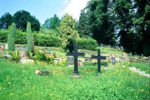 Blick auf den Friedhof; im Vordergrund zwei Metallkreuze