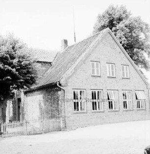 Volksschule: Kreisstraße in Richtung Reinfeld: links Zaun an Schulgebäude: hinten rechts und links Bäume