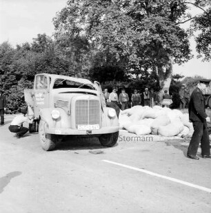 B 75: bei Reinfeld, Höhe Herweg: Unfall-Lkw mit eingedrückter Karosserie und geöffneten Türen: Polizist in Hocke bei Untersuchung des Wagens: an Straßenrand viele gefüllte Säcke von verlorener Ladung: rechts Polizist: hinten Schaulustige, Hinweisschild zur Autobahn, Baum, Büsche