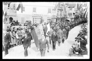 Umzug von Männern in Zivil durch die mit Reichsflaggen geschmückte Brückengasse
