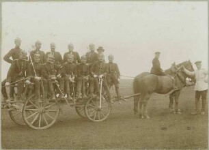 12 Soldaten in Uniform und Pickelhaube, ein Zivilist mit Hut auf Pferdefuhrwerk teils stehend, teils sitzend auf Truppenübungsplatz bei Münsingen