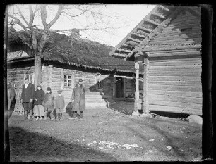 Unbekannte Ortschaft [Rumänien?]: einheimische vierköpfige Familie und ein weiterer Mann vor einem reetgedeckten Holzhaus (Distanzaufnahme)