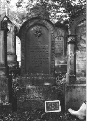 Grabstein 552 (Index: 99895431) Material: Sandstein Zustand: gut, Sockel verwittert Maße HxBxT: 174x56x20 cm Beschreibung: Stele mit Rundbogenabschluss, kleiner Verdachung und Mittelakroter; Sockel Symbolik: Blüte: Grabstein 552 (1)