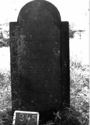 Grabstein 945 (Index: 100103845) Material: Sandstein Zustand: gut erhalten Maße HxBxT: 133x60x9 cm Beschreibung: Stele, eingezogener Rundbogenabschluss, Schriftfeld eingetieft mit Konvexbogenabschluss, Buchstaben wirken unprofessionell (unterschiedliche Größen): Grabstein 945