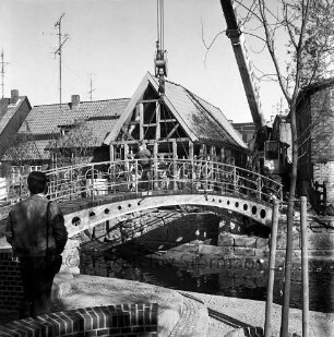 Trave: Stadtarm: Bau der Brücke zwischen der Hude und Heiligengeiststraße: ein Krangerät hebt die Brücke ein, vorne und auf der Brücke Personen, im Hintergrund Gebäude der Heiligengeiststraße, Blick nach Nordwesten
