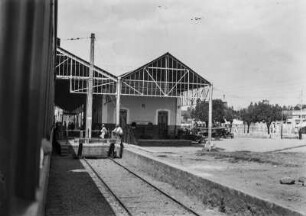 Bahnhof in Americana : Blick aus einem Zug am Bahnhof in Americana mit der Sicht auf das Bahnhofsgebäude und auf Passagiere am Bahnsteig.