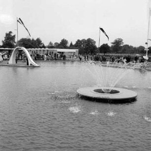 Sommerbad Tarpenbek: Am Hallenbad: Eröffnung: Nichtschwimmerbcken mit Springbrunnen (vorne) und Wasserrutsche, Gäste am Beckenrand, im Hintergrund Sanitäranlagen