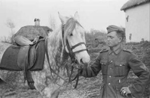 Zweiter Weltkrieg. Zur Einquartierung. Sowjetunion. Angehöriger der deutschen Wehrmacht mit Reitpferd