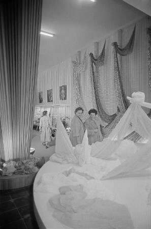 Besucher der Leipziger Herbstmesse 1955 betrachten drapierte Stoffbahnen