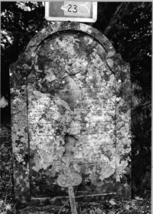 Grabstein 23 (Index: 100090620) Material: Sandstein Zustand: abgeblättert/verwittert mit Textverlust Maße HxBxT: 93x60x9 cm Beschreibung: Stele, doppelt eingezogener Segmentbogenabschluß, Schriftfeld eingetieft: Grabstein 23