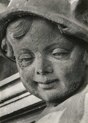 Putto mit Päckchen und Geldbeutel. Um 1905. Sandstein. Figur auf dem Ständehaus, Detail Gesicht während der Substanzsicherung/Wiederaufbau Dach. Dresden-Altstadt, Schloßplatz 1