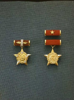 Staatliche Auszeichnungen der Deutschen Demokratischen Republik. Links: Goldener Stern, Medaille zum Ehrentitel "Held der Deutschen Demokratischen Republik" an Spange. 2. Modell mit 5 Brillanten (Verleihung 1977/1982). Gold (900er), Brillanten. Spange in Gold, rot bezogen, mit 3 Brillanten besetzt. Rechts: Orden "Held der Arbeit" in Gold mit Spange und Interimsspange. Stern mit Staatsemblem der DDR (Ausführung der 2. Form). Stoff (rot), Metall, vergoldet; 34 x 34 mm, Spange 10 x 31,5 mm. Ab 1952, gestiftet am 19.4.1950