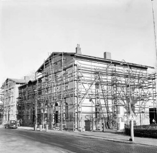 Bahnhofsgebäude: Streichen der Fassade: mit Gerüst und Leitern: rechts Litfaßsäule, Straßenlampe, Verkehrsschild: vorne Bahnhofstraße, Mülltonnen, links parkender Pkw