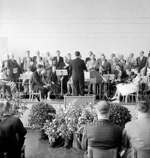 Tag der Deutschen Einheit: Feierstunde: Veranstalter Kuratorium "Unteilbares Deutschland": Theodor-Mommsen-Schule: Hamburger Straße: Festsaal: Blick von Empore: Bürgerworthalter Willy Rosch hält Ansprache: auf der Bühne Orchester der Theodor-Mommsen-Schule und Männerchor: Fahne der Bundesrepublik Deutschland, Fahne der Stadt Berlin: Gäste, 17. Juni 1961