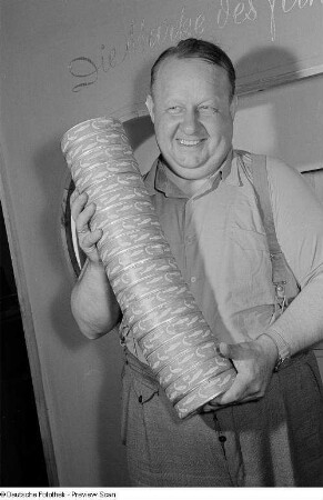 Ein Mann präsentiert aufeinander gestapelte Fischdosen auf der Leipziger Herbstmesse 1954