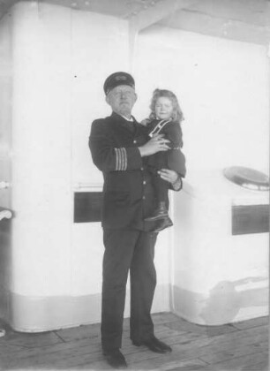 Kreuzfahrten der Hamburg-Amerika Linie, um 1911/1913. Porträt des Kapitäns (?) eines Hochseepassagierdampfers mit einem kleinen Mädchen auf dem Arm an Bord