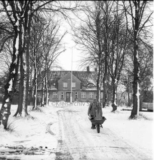 Bauerngehöft Peter Hinselmann: Zufahrtsallee mit Baumreihen: im Vordergrund Mann mit Schubkarre: Winter