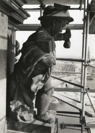 Putto mit Päckchen und Geldbeutel. Um 1905. Sandstein. Figur auf dem Ständehaus, Seitenansicht mit Gerüst während der Substanzsicherung/Wiederaufbau Dach. Dresden-Altstadt, Schloßplatz 1