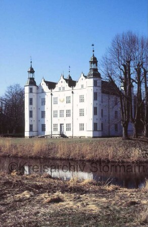 Schloss Ahrensburg: Ansicht von Südosten: Südfassade mit angrenzenden Türmen: an mittlerem Giebelhaus Sonnenuhr: Gartenportal, Gartenbrücke über inneren Schlossgraben: rechts Lindenreihe: im Vordergrund äußerer Schlossgraben