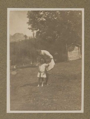 Hugo von Hofmannsthal mit seinem Sohn Raimund im Garten vor Bergen stehend, sich zum Kind hinunterbeugend