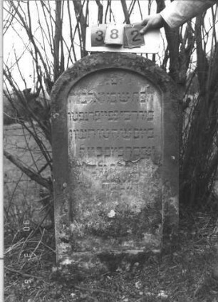 Grabstein 382 (Index: 99609106) Material: Sandstein Zustand: sehr stark verwittert mit Textverlust Maße HxBxT: 115x61x11 cm Beschreibung: Stele, Rundbogenabschluß, Schriftfeld eingetieft in gleicher Form: Grabstein 382