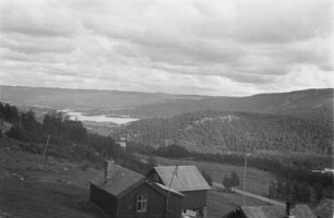 Landschaft : Hügelige Landschaft. Im Bildvordergrund eine unbekannte Siedlung. Im Bildhintergrund ein See.