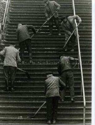Sechs Männer mit Schaufeln reinigen eine Treppe