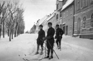 Erzgebirge. Drei Skiläufer auf einer Straße in einer Stadt. Blick gegen Wohnhäuser