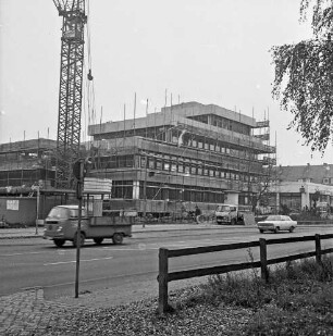 Gemeindeverwaltung: Rathaus: Hauptstraße mit Bauwagen und Pkw: Neubau vor Fertigstellung mit Gerüsten: davor Fußgänger und Fahrradfahrer: rechts Bauwagen: links Kran: im Vordergrund rechts Zaun: rechts oben Baumäste