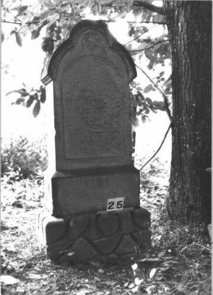 Grabstein 25 (Index: 99898731) Material: Sandstein Zustand: fast völlig verwittert Maße HxBxT: 148x57x29 cm Beschreibung: aufgesockelte Stele mit seitlich auskragendem Dreipassbogenabschluss, im Bogen Blüte, unterer Sockel felsartig gearbeitete, Schrift mit schwarzer Farbe nachgezogen Symbolik: Blüte: Grabstein 25